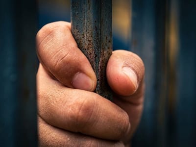 Hand gripping a rusted metal bar of a jail cell
